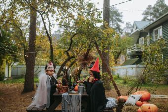 Children in costumes enjoy a Halloween party outdoors with decorations and pumpkins.