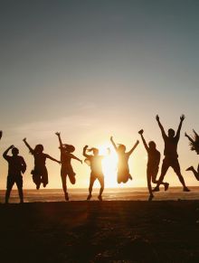 Silhouette of a group of friends jumping on a beach at sunset, expressing joy and freedom.