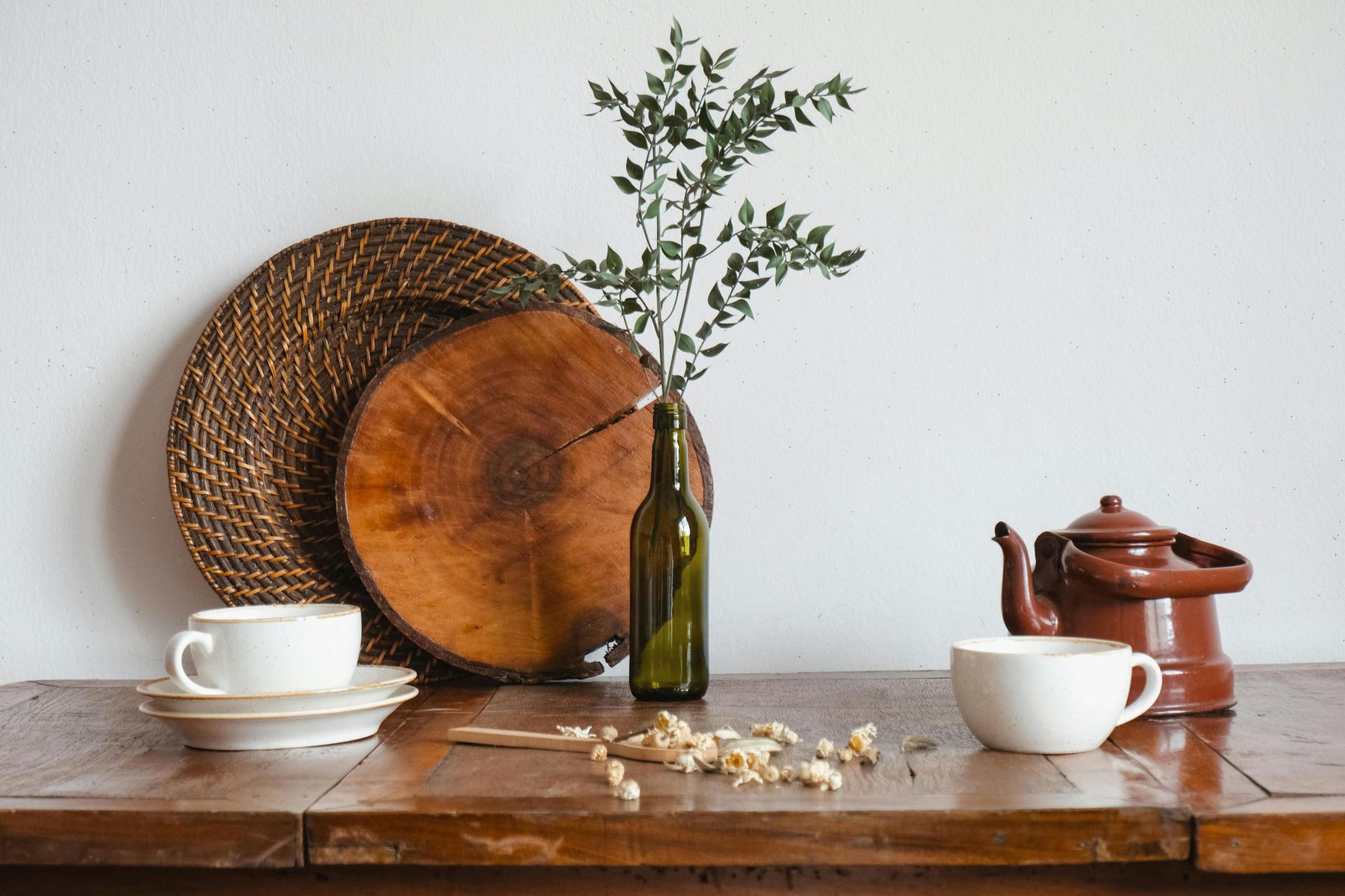 A cozy still life of tea cups, teapot, and rustic decor on a wooden table.