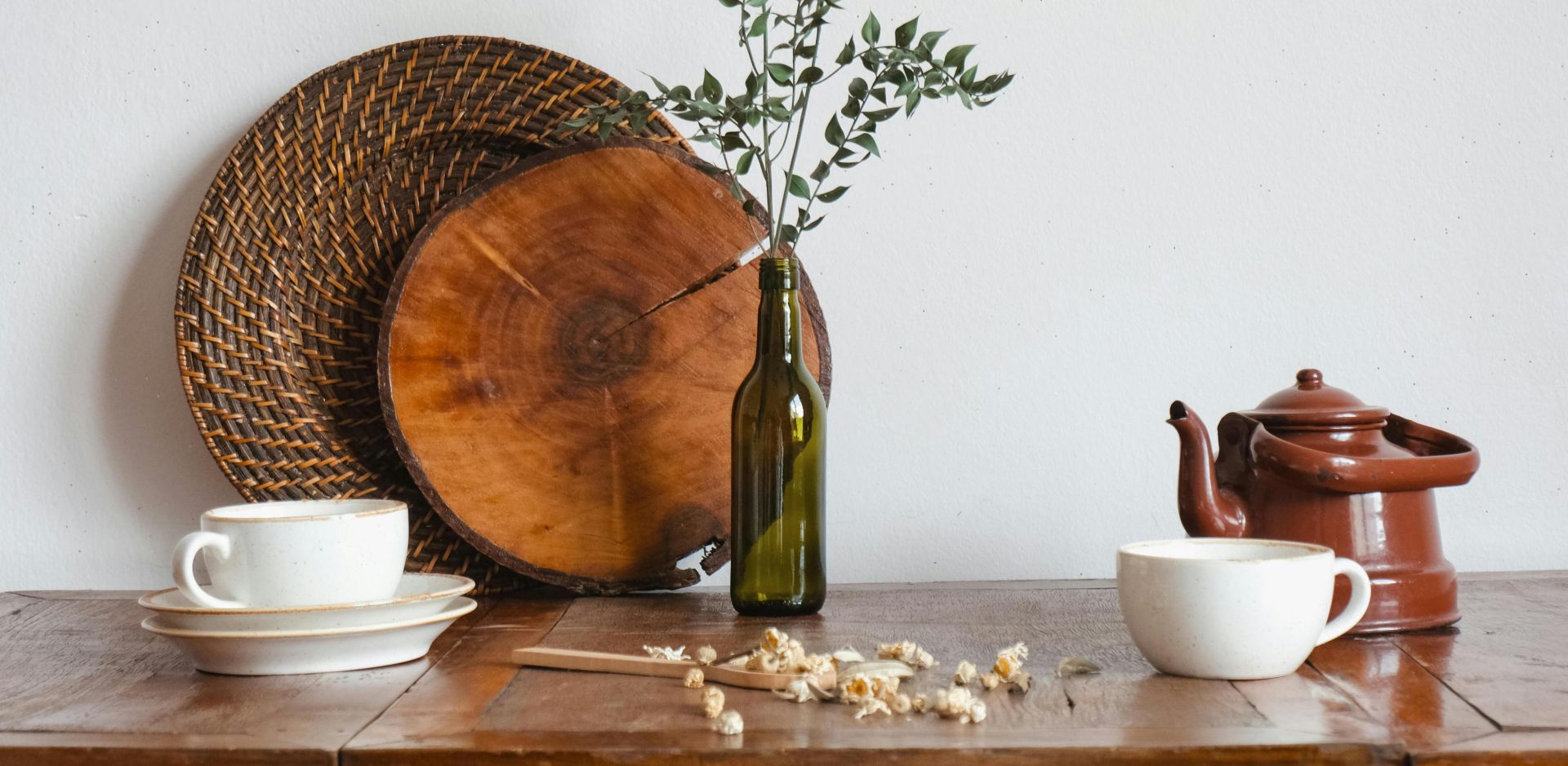 A cozy still life of tea cups, teapot, and rustic decor on a wooden table.